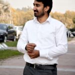 A man in a white shirt standing outdoors, exuding confidence.